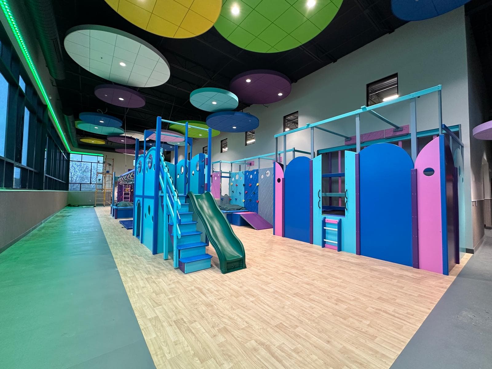 Fun Factory commercial sensory gym with colorful ceiling discs, blue playhouse structures, green slide, and climbing walls