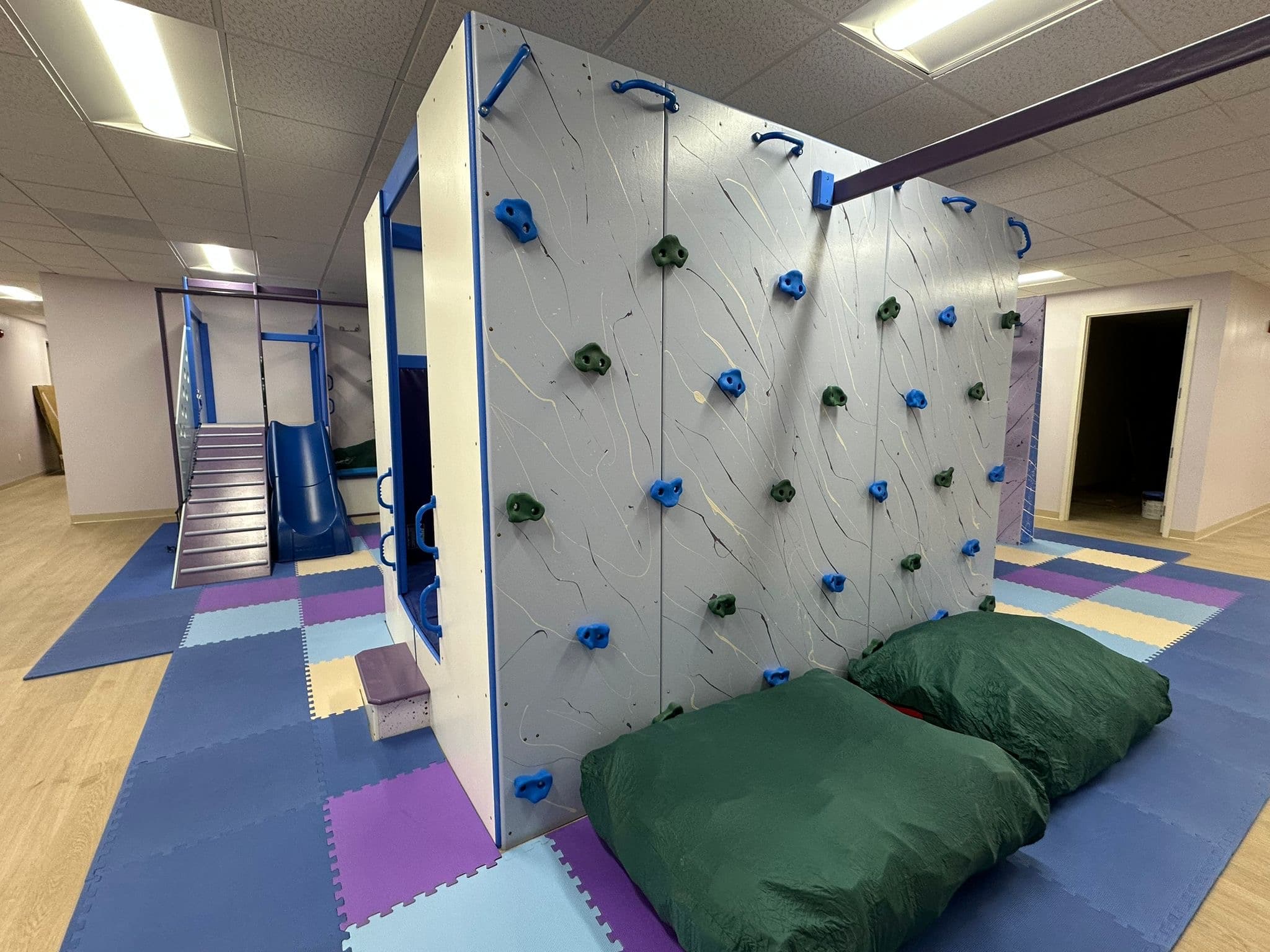 Clinic climbing structure with white rock wall, blue and green holds, and green crash pillows