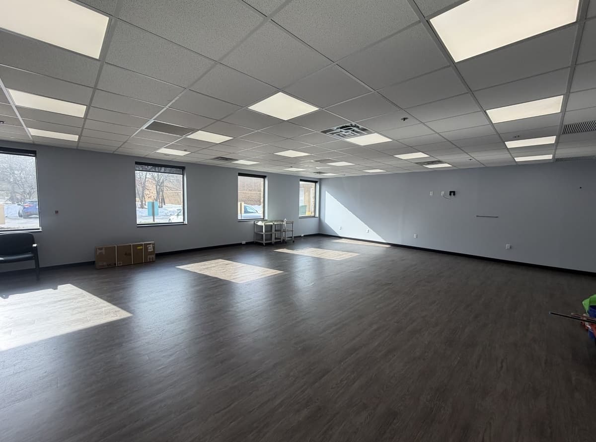 Before: empty clinic room with drop ceiling and dark wood-look floor, ready for a sensory gym