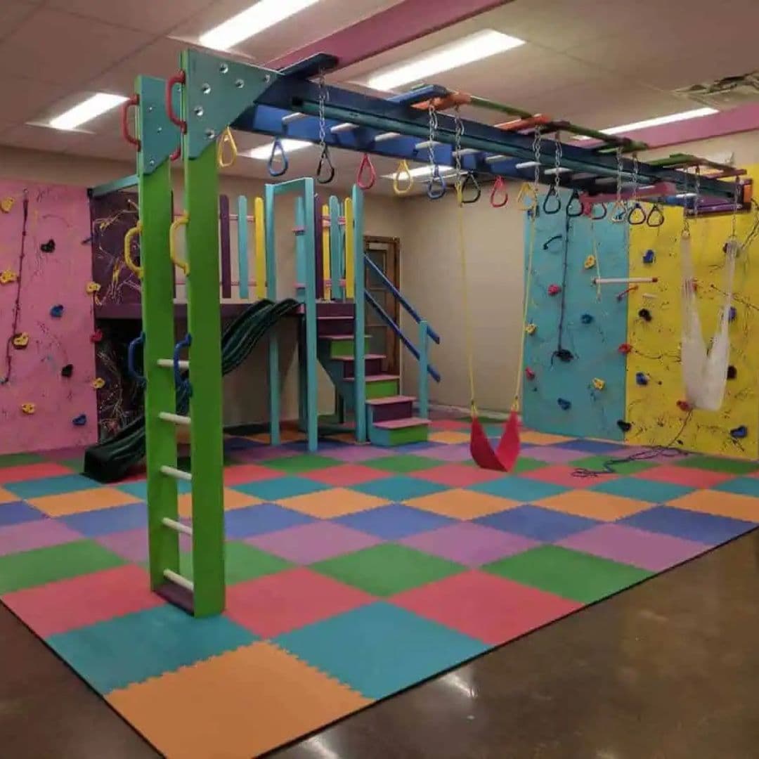 Full commercial sensory gym build with overhead monkey bar track, green ladder, and rainbow foam floor