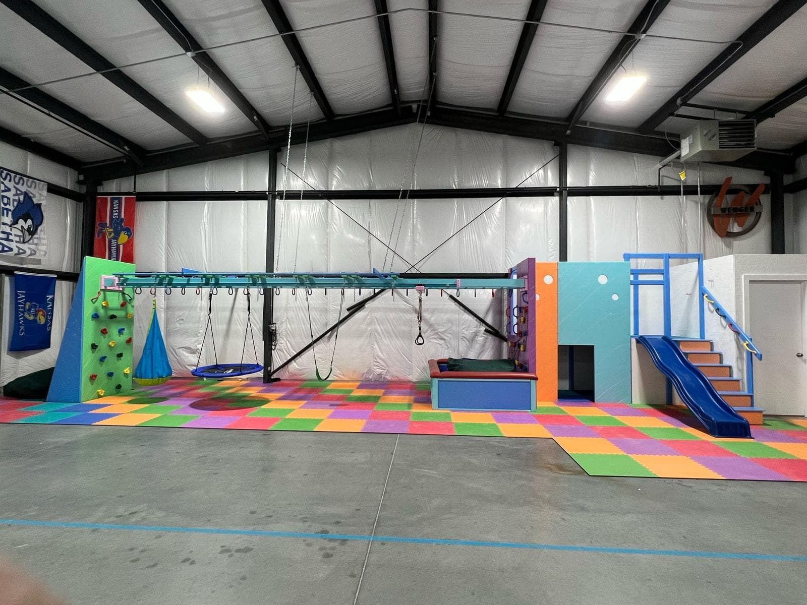 Home garage converted into a sensory gym with climbing wall, swings, blue slide, and rainbow foam floor