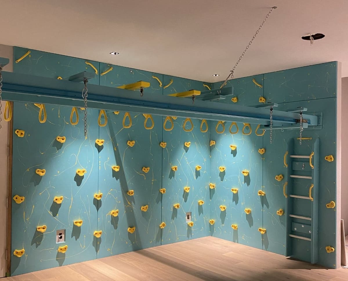 After: teal climbing wall with yellow holds and overhead trapeze track installed by Fun Factory