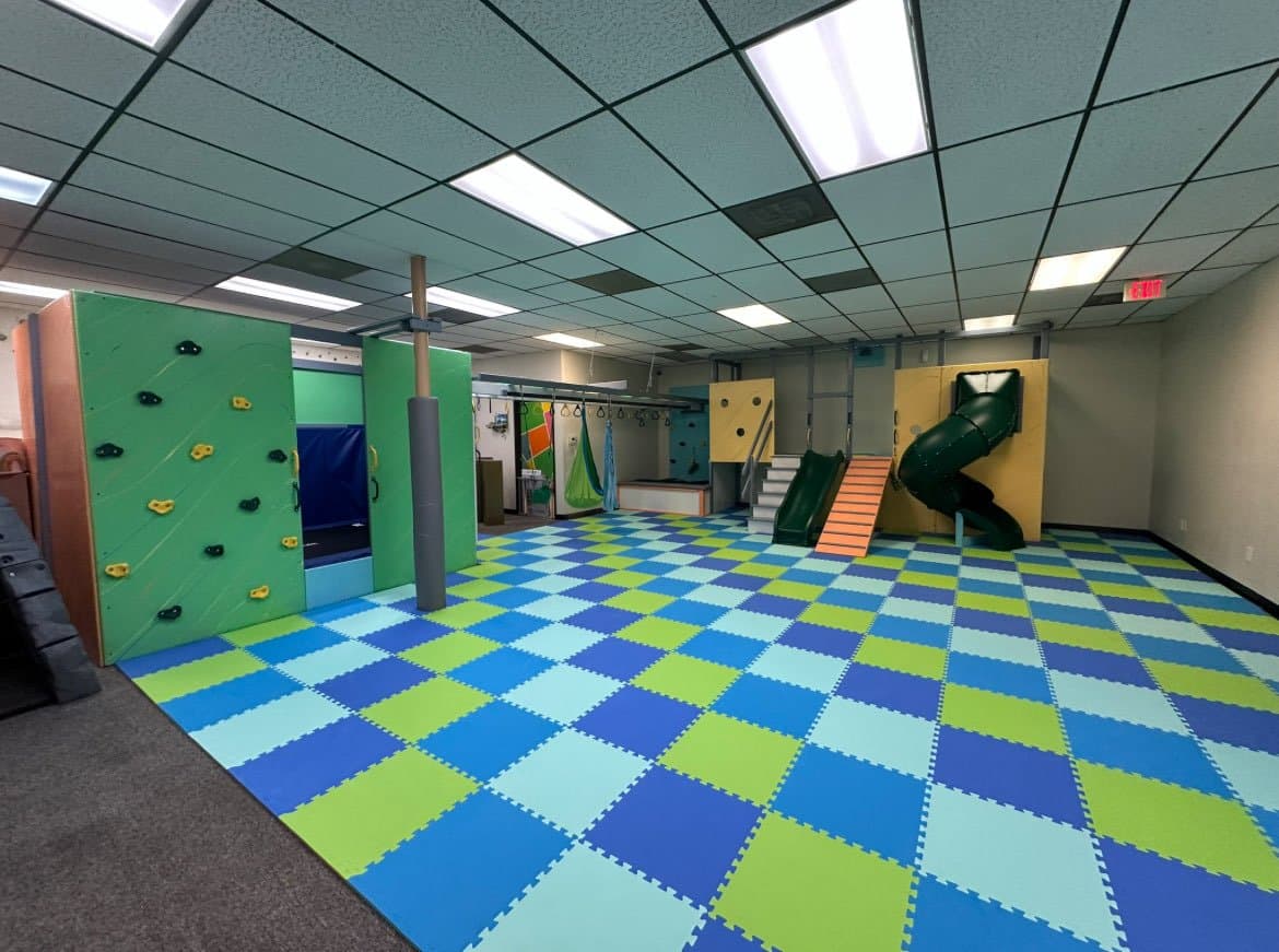 Fun Factory sensory gym installation with green climbing wall, green tube slide, and blue and green foam floor